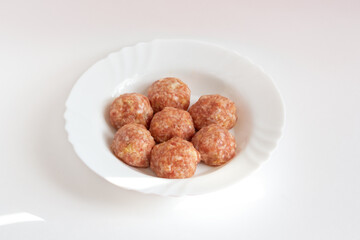 A few raw noisettes lie on a white plate. Raw meat balls with rice, spices, sauce, finely chopped cabbage are ready for cooking