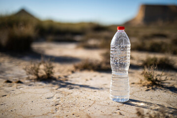 Unlabeled plastic water bottle on arid soil into desertic landscape with copy space