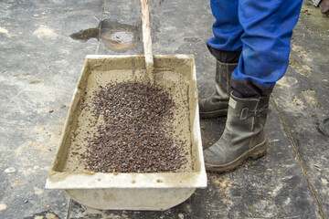 A man in blue pants and black leather boots stirs a cement mortar with a snub. Small gravel was poured into the concrete. Construction work without the help of special equipment.