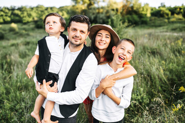 Midshot of a happy family outside on nature. A capture of a happy family of a dad and mom and two theirs sons standing in the middle of a green field in smart casual wear