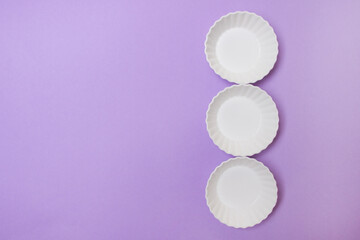 three empty white plate on purple colored paper background with copy space