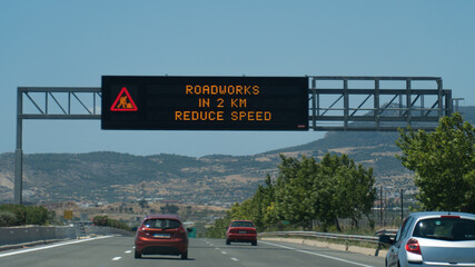 Road sign in Greek highway with message on electronic display: roadworks in 2 km reduce speed