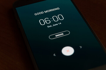 On a black smartphone, an alarm clock rings for 6 am with the inscription Good morning close-up,...