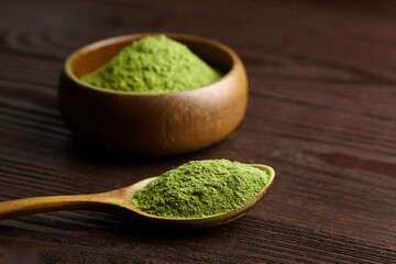 Dried organic wheat or barley grass powder heap in spoon andd bowl on dark wooden background.
