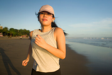 Asian girl running on the beach - young attractive and happy Korean woman doing jogging workout at beautiful beach enjoying fitness and healthy runner lifestyle