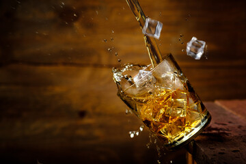 Falling glass with whiskey and ice with splashes on an old wooden table