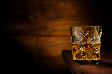 Half a glass of whiskey with ice cubes on an old wooden table, rustic style