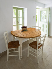 A simple white kitchen table with wooden surface and white chairs in a country house with door and window to the garden.