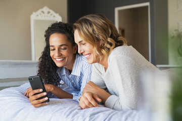 Happy women friends using phone at home