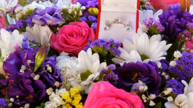 Top view of gift present red box with a set of engagement ring and earrings on the background of a multi-colored beautiful bouquet of flowers. Marriage proposal, a new happy life
