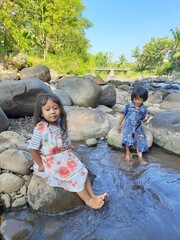 Asian kid girls are standing and playing on the river and rocks in the beautiful village.they are on vication