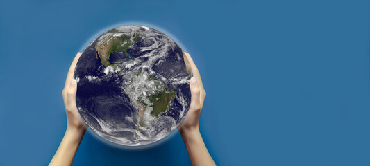 The concept of the environment, the world in your hands. Two female hands hold a globe with an image of the earth on a blue isolated background. Copy space, top view, selective focus, banner.
