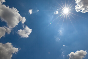 Naklejka na ściany i meble Słońce z promieniami na tle błękitnego nieba z chmurami.