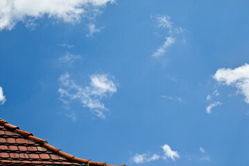 Fragment dachu na tle błękitnego nieba z chmurami.