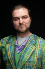 low key portrait of confident good looking bearded man in green blazer looking at camera isolated on black