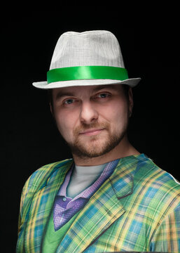 handsome bearded confident man in grey stylish hat with green ribbon and checkered coat looking at camera on black 