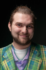 low key portrait of smiling good looking bearded man in green blazer looking at camera isolated on black