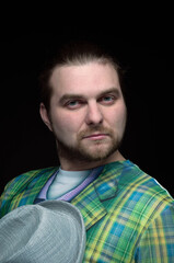 Fototapeta premium low key portrait of confident good looking bearded man in green blazer looking at camera and holding grey hat isolated on black