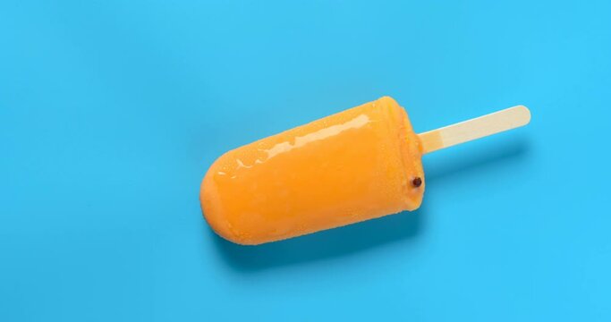 top view orange color chocolate outer popsicle with beans inside melting timelapse on blue background