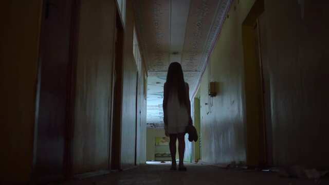 a girl with long black hair and a white dress is walking slowly in a dark corridor. The concept of a horror maniac. Halloween. she is holding a Teddy bear,