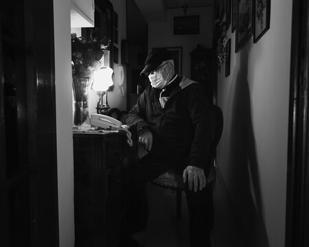 Covid-19 Black And White Frontal View Full Body Portrait Of An Old Man Sitting On A Chair Waiting A Call On The Phone