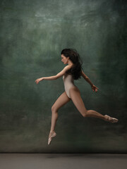 Coming on. Graceful classic ballerina dancing on dark studio background. Pastel bodysuit. The grace, artist, movement, action and motion concept. Looks weightless, flexible. Fashion, style.