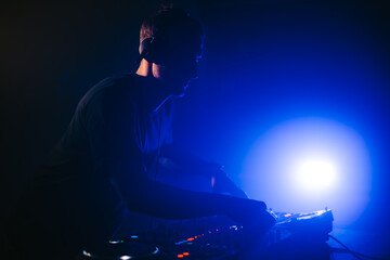 DJ spinning in a night club at a party with dark blue lights.