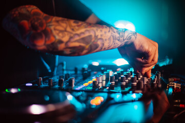 Horizontal shot of a tattooed arm of a young caucasian male DJ who with his hand is turning the...