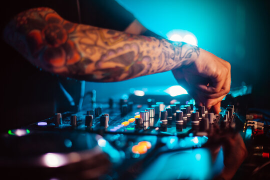 Horizontal shot of a tattooed arm of a young caucasian male DJ who with his hand is turning the buttons on the mixer