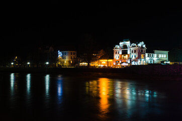 Obraz premium Night city photographed at long exposure. Water, glare and night lights. Architecture and buildings of the city of Uzhgorod. Beautiful night photos without people. No one is on the street.