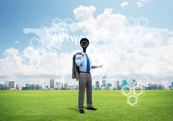 Camera headed man standing on green grass against modern cityscape