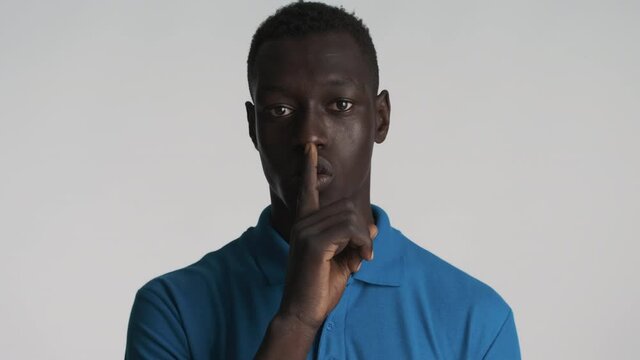Young attractive African American man confidently showing silence gesture on camera over gray background. Shh expression