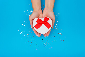 Women hands holding a gift or gift box decorated with confetti on a blue table top view.
