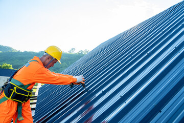 Roofer worker in special protective workwear use electric drill installing new roofs with metal...