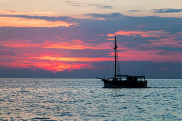 ship sailing with the last lights of the day. Sunset in Piran, Slovenia. Backlight of a boat