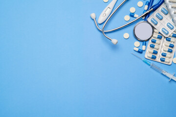 blister of pills capsiles, thermometer, syringe and stethoscope isolated on blue background