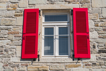 An wood vintage window with red shutters on the  stone wall