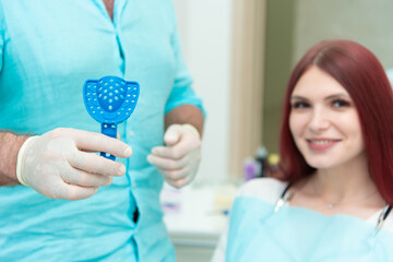 The orthodontist shows the patient an impression tray in which the silicone impression material will be placed to get the shape of her teeth