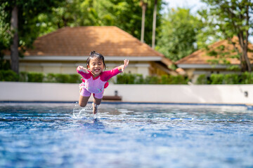 Little girl with pink swim suit jumping into swimming pool in summer.