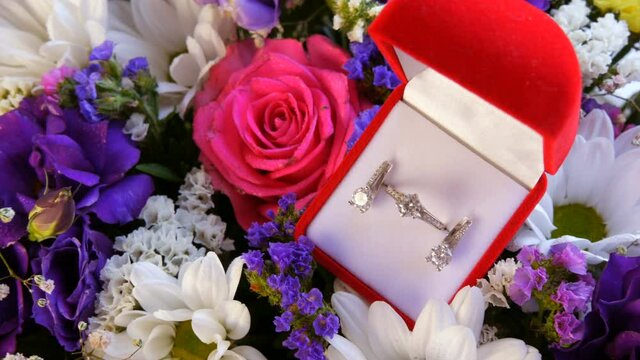 Top view of gift present red box with a set of engagement ring and earrings on the background of a multi-colored beautiful bouquet of flowers. Marriage proposal, a new happy life