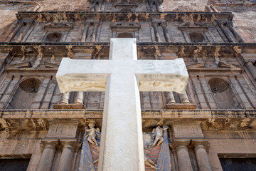 White cross Christian religious symbol, detail with unfocused facade background.