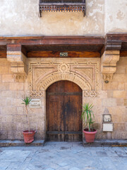 Fototapeta na wymiar Facade of old stone bricks decorated wall with arched wooden door, Entrance of old Ottoman historic house of Moustafa Gaafar Al Selehdar, Moez Street, Old Cairo, Egypt