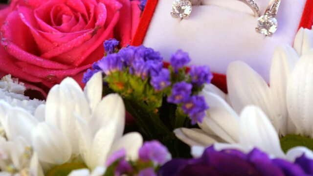 Close up view of gift present red box with a set of engagement ring and earrings on the background of a multi-colored beautiful bouquet of flowers. Marriage proposal, a new happy life