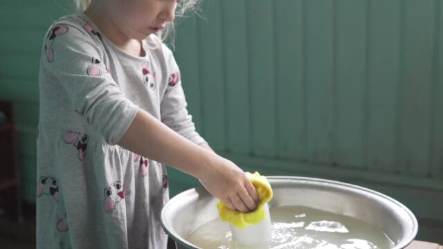 Cute little girl washes to mud a cup in the trough with water on dace. The life of Children in Russian Wood