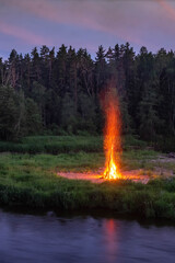 Traditional midsummer Ligo celebration. Huge bonfire on the river shore. Scenic landscape of forest at twilight.