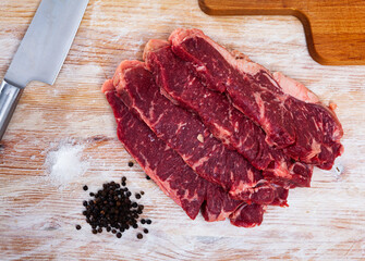 Sliced raw marbled veal steaks with peppercorns ready to cook on wooden table