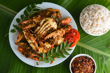 Chili crab curry or Kerala crab roast and rice, popular hot and spicy seafood dish in India, Sri Lanka, Singapore. Woman hand cooking roasted coconut sauce on dark background.