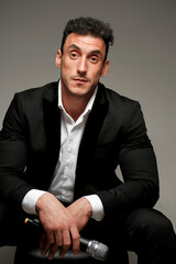 Close up portrait of a man 30-34 years old in a white shirt and black jacket on a gray background. A man holds a microphone in his hand.