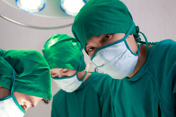 Fototapeta na wymiar Medical Team Performing Surgical Operation in Bright Modern Operating Room, Doctor male looking at the camera. Close up doctor in green surgery gown.