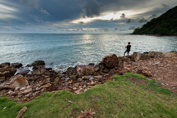 Fototapeta na wymiar A man fishing during coastal sunset with rocky coastline and texture of cloudy sky in Chanthaburi province, Thailand